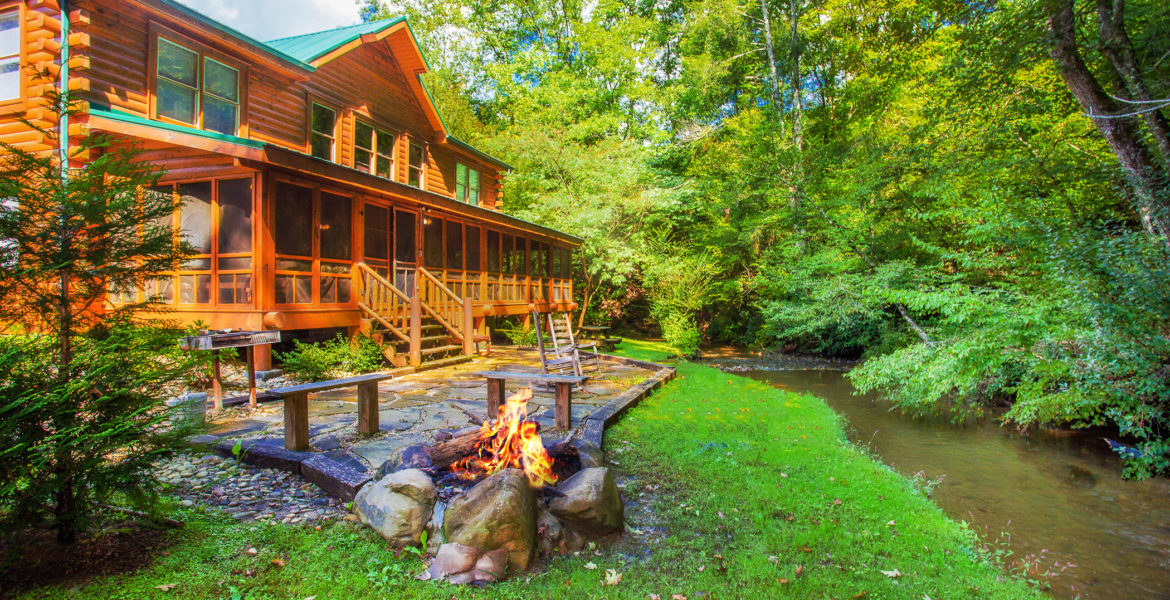 large cabin next to a river with a fire pit and patio